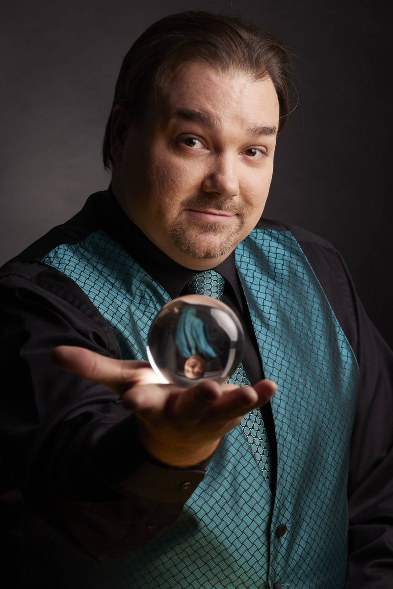 Close-up of a confident man holding a glass orb, reflecting his image, showcasing professional portrait photography.